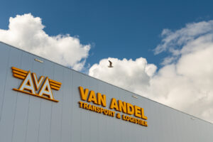 Korteland In- en Outdoor Signing Van Andel gele lichtgevende letters op grijs gebouw blauwe licht wolken